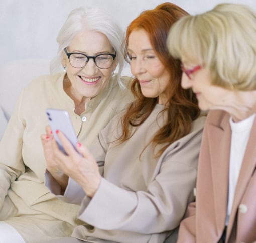 three women smiling while looking at a phone